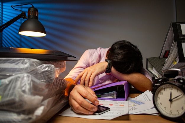 Pracownik biurowy tajski senny personel spać na biurku po zakończeniu raportu w nocy.