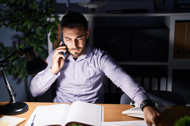 Pracownik biznesowy młody latynoski rozmawia przez smartfon pracujący w godzinach nadliczbowych w biurze