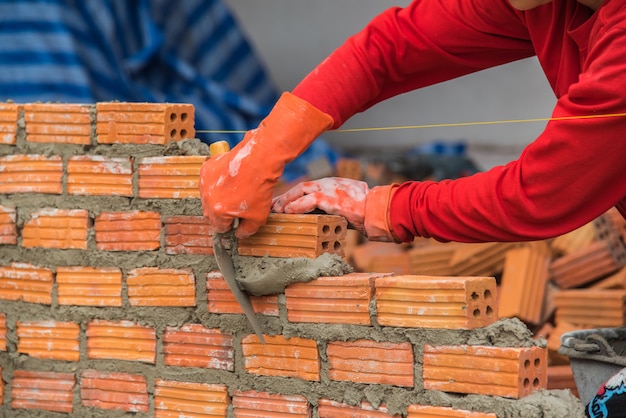 Pracownik budowlany kłaść cegły i budować ścianę w przemysłowym miejscu.