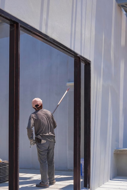 Pracownik budowlany nakładający białą farbę podkładową na ścianę cementową wewnątrz budowy domu