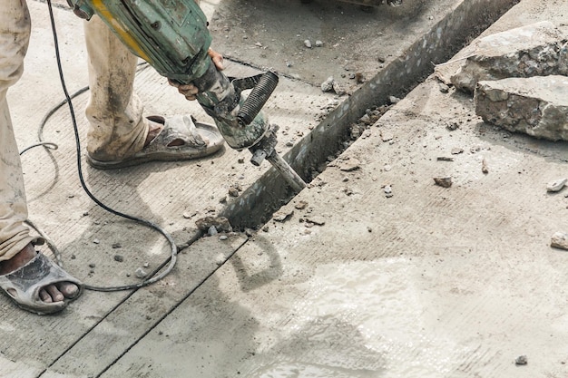 Zdjęcie pracownik budowlany za pomocą młota pneumatycznego wiercenia powierzchni betonu