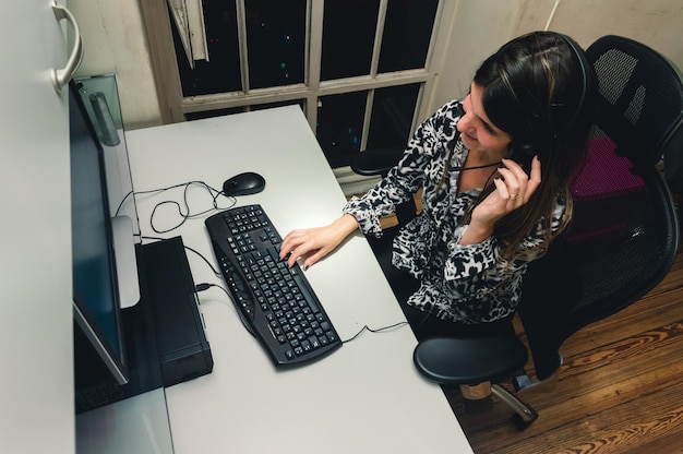 Pracownik centrum telefonicznego kobiet pracujący jedną ręką na zestawie słuchawkowym i oglądający komputer