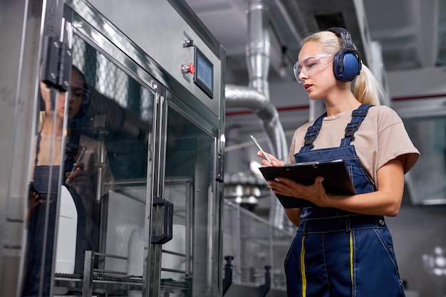 Pracownik fabryki przeprowadza kontrolę jakości w pracy, robi notatki w teczce-tablecie, zapisuje informacje o sprzęcie robota. pracownik w mundurze ochronnym pracujący w badaniach zaopatrzenia medycznego