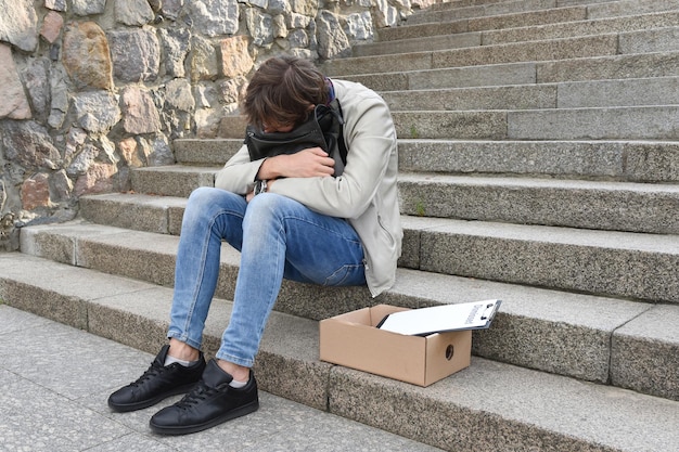 Pracownik firmy, który stracił pracę, siedzi na schodach na ulicy w ciężkiej depresji
