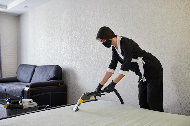 Pracownik firmy usług sprzątania usuwa zabrudzenia z mebli w mieszkaniu z profesjonalnym sprzętem Gospodyni sprzątająca materac na łóżku odkurzaczem piorącym