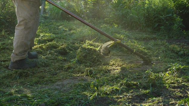Pracownik kosi trawę ręczną kosiarką gazową Cięcie chwastów z bliska Czyszczenie terytorium z chwastów przez ogrodnika