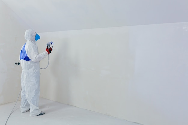 pracownik maluje ścianę rozpylaczem w nowo wybudowanym domu