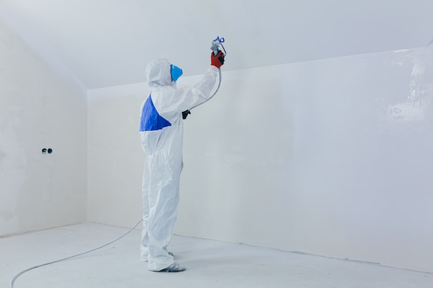 pracownik maluje ścianę rozpylaczem w nowo wybudowanym domu