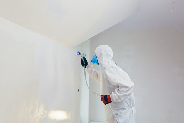 Pracownik maluje ściany pistoletem natryskowym w nowym budynku