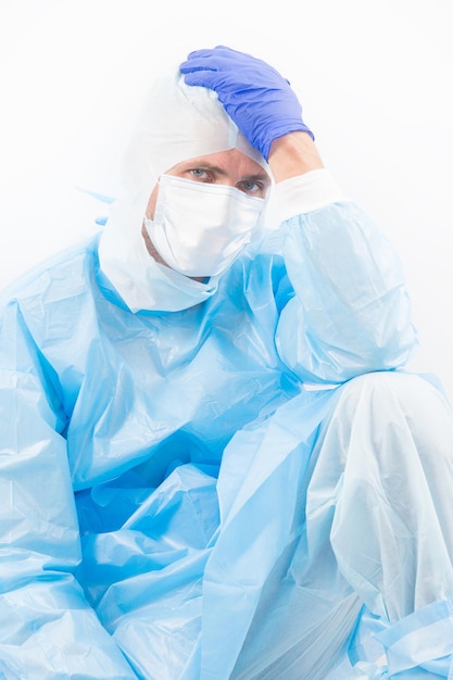 Pracownik medyczny mężczyzna w stroju ochronnym na białym tle mający objawy wirusa covid19 sars bólu głowy, pandemii koronawirusa.