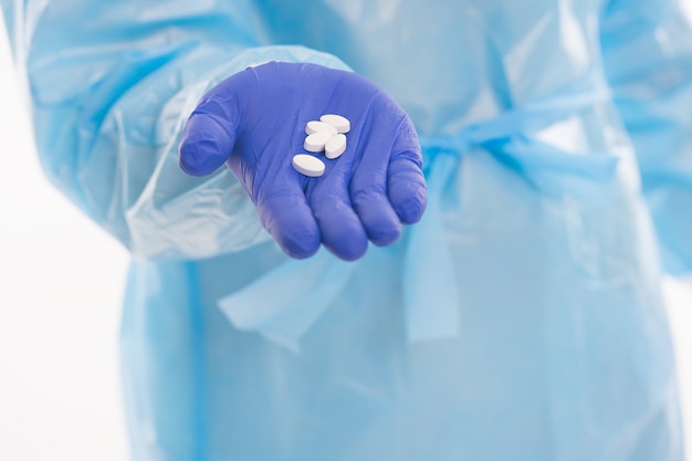 Pracownik medyczny w stroju ochronnym na białym tle oferuje antybiotyki w tabletkach na leki