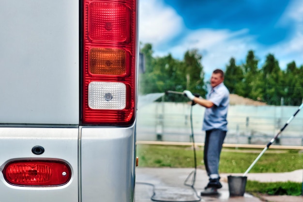 Pracownik myjni ręcznie myje duży autobus strumieniem wody na otwartym parkingu w letni dzień