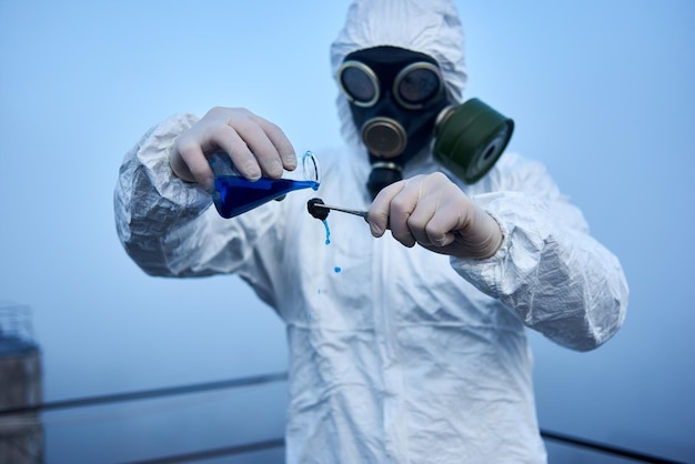 Pracownik naukowy w kombinezonie ochronnym i masce przeciwgazowej przeprowadzający testy ekologiczne na dachu