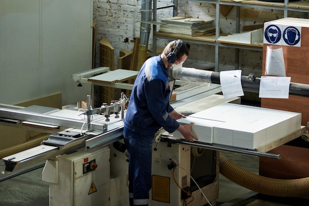 Zdjęcie pracownik obrabia półfabrykaty mebli na obrabiarce w fabryce. produkcja przemysłowa mebli.
