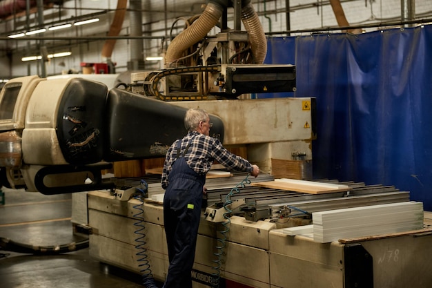 Pracownik obrabia półfabrykaty mebli na obrabiarce w fabryce. Produkcja przemysłowa mebli.