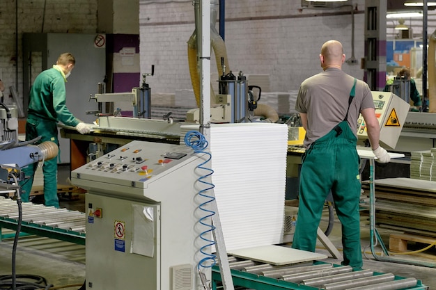 Zdjęcie pracownik obrabia półfabrykaty meblowe na złożonej maszynie technologicznej w fabryce. produkcja przemysłowa mebli.