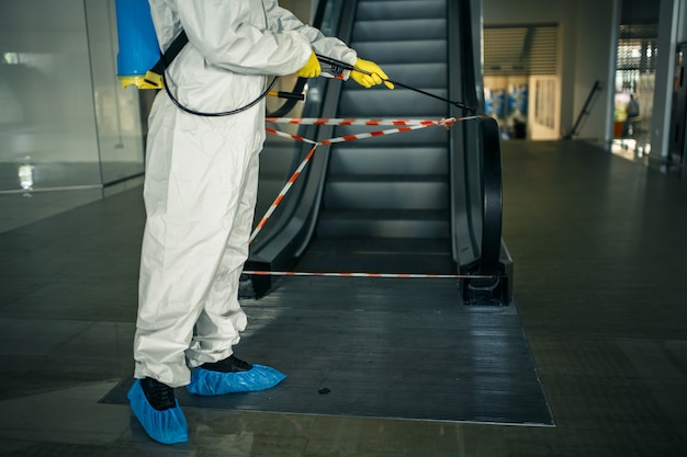 Pracownik odkażający dezynfekuje schody ruchome za pomocą sprayu w pustym centrum handlowym, aby zapobiec rozprzestrzenianiu się COVID-19 w miejscach publicznych.