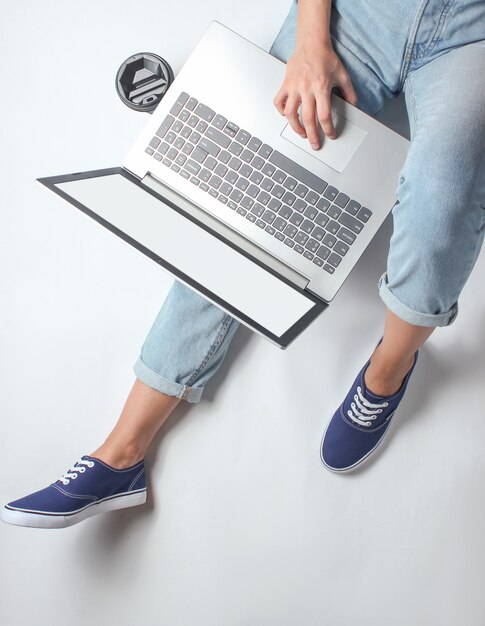 Zdjęcie pracownik online w miejscu pracy. fragment kobiecych nóg w dżinsach i trampkach. kobieta siedzi i używa laptopa. koncepcja niezależna. praca w domu.