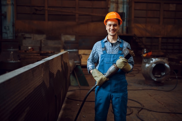 Pracownik płci męskiej w mundurze i kasku pracuje z metalowymi przedmiotami w fabryce. Przemysł metalowy, produkcja przemysłowa wyrobów stalowych