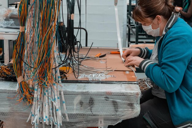 Zdjęcie pracownik przemysłowy noszący maskę na twarz z powodu pandemii koronawirusa lutuje kable z fabrycznego sprzętu produkcyjnego. wysokiej jakości zdjęcie