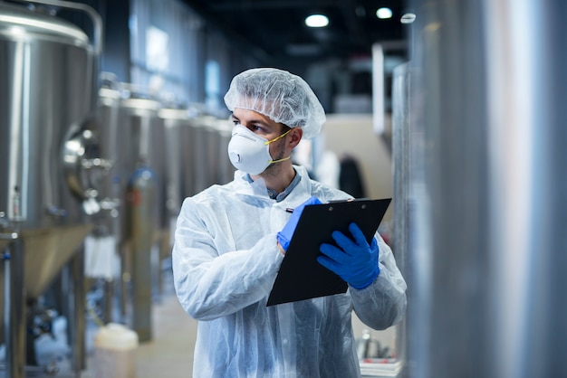 Pracownik przemysłowy noszący maskę ochronną i białe ubranie posiadający listę kontrolną w fabryce.