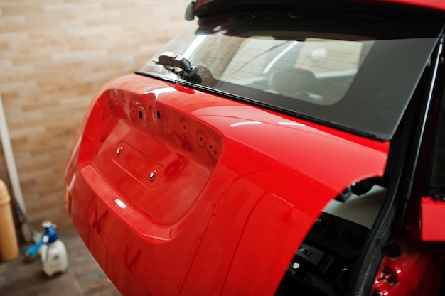 Pracownik serwisu samochodowego nałożył folię przeciw żwirowi na karoserię w kolorze czerwonym w warsztacie samochodowym detailingowym Zabezpieczenie samochodu specjalnymi foliami