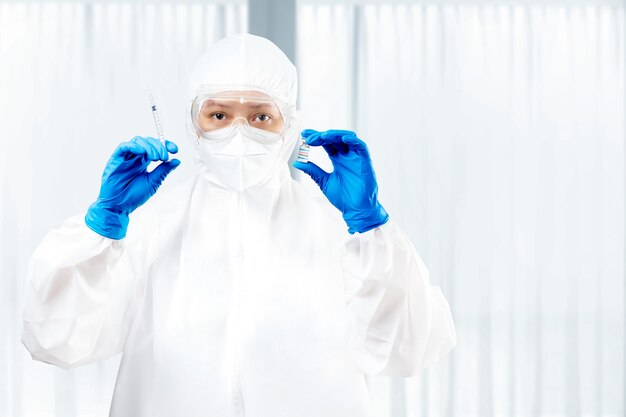 Pracownik służby zdrowia kobieta w kombinezonie ochronnym i rękawiczkach trzymająca covid 19 szczepionek w szpitalu
