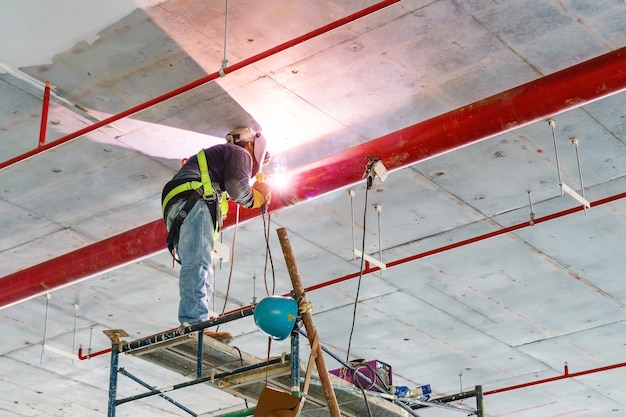 Pracownik spawalniczy czerwieni drymby obwieszenie od sufitu wśrodku niedokończonego nowego budynku