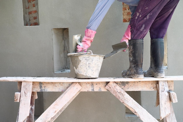 Pracownik stoi na drewnianych rusztowaniach i nakłada cement na placu budowy