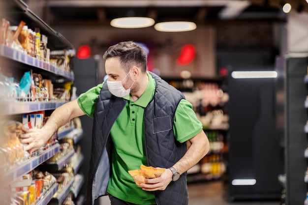 Pracownik supermarketu wystawiający artykuły spożywcze w przejściu podczas covid 19