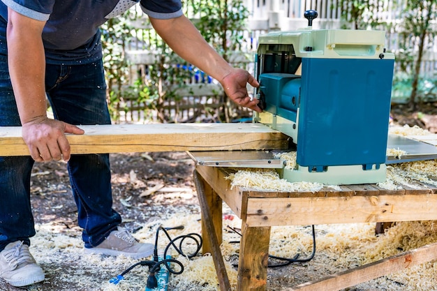 Pracownik szoruje dużą długą drewnianą płytę za pomocą maszyny do polerowania w ogrodzie