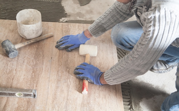 Zdjęcie pracownik trzymający młotek gumowy. układanie podłogowych płytek ceramicznych. renowacja podłogi