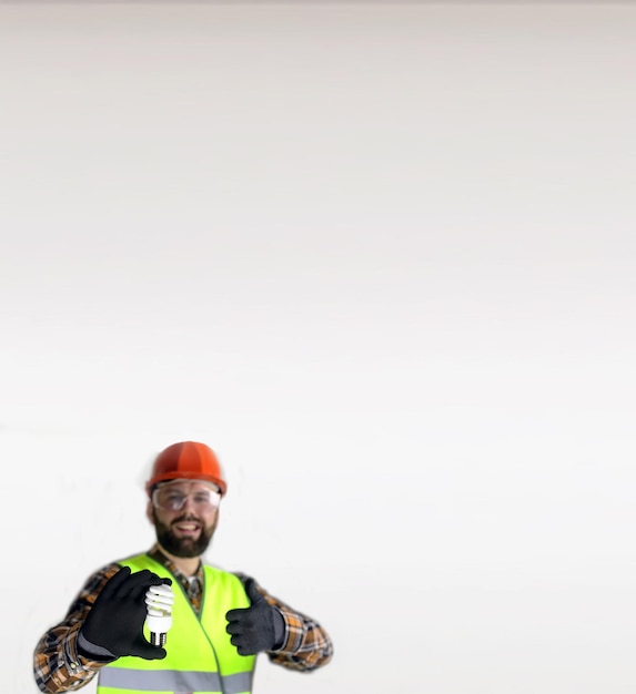 Pracownik w kasku i odzieży ochronnej z żarówką w rękach na szarym tle
