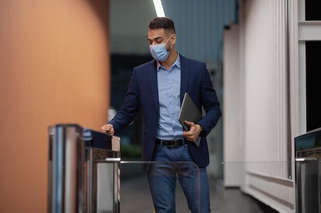 Pracownik w masce na twarz trzymający laptopa przechodzący przez bramę wejściową