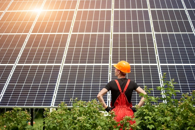 Pracownik w pomarańczowym mundurze stoi tyłem do aparatu na tle dużej plantacji baterii słonecznych