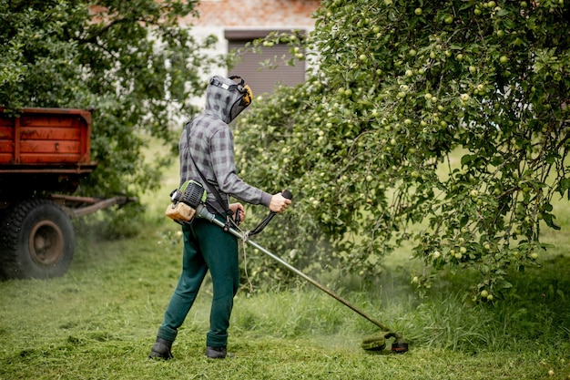 Zdjęcie pracownik z kosiarką gazową w rękach, koszący trawę przed domem