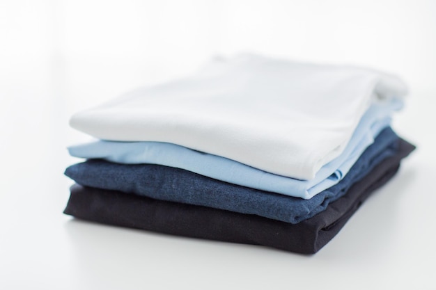 prasowanie, pranie, ubrania, sprzątanie i koncepcja przedmiotów - zbliżenie wyprasowanych i złożonych koszulek na stole w domu