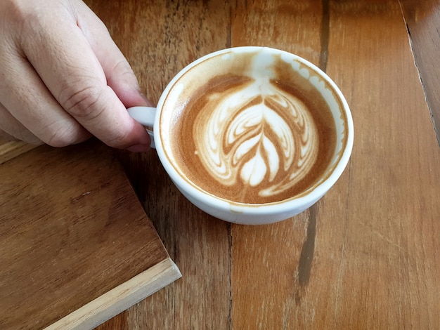 Prawa ręka kobiety trzymającej filiżankę gorącej kawy latte art na drewnianym tle