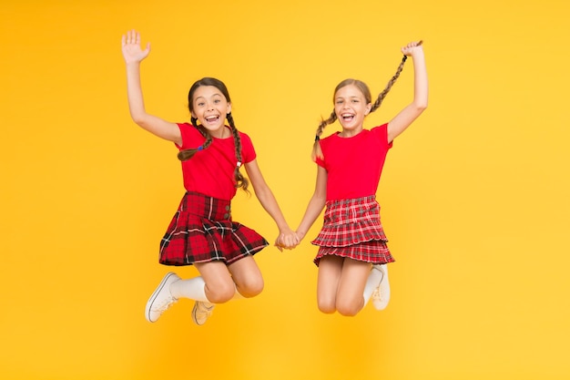 Prawdziwa radość szczęśliwe dziewczynki w kraciastej spódniczce uroda wyglądają szczęśliwe dzieci na żółtym tle szczęście dzieciństwa modny mundurek szkolny zabawny skok czerwony moda dziewczyny angielski styl moda