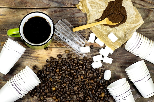 Zdjęcie prażone ziarna kawy z proszkiem i jednorazowymi kubkami i cukrem z plastikową łyżką na drewnianym stole