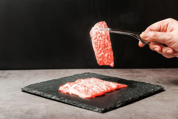 Premium Rare Slices Polędwica Wołowa Wagyu A5 O Wysokiej Marmurkowej Teksturze Zbierana Szczypcami Do Grillowania Ręką Z Kamiennej Płyty Podawane Dla Yakiniku Sukiyaki I Shabu Image Z Miejscem Na Kopię