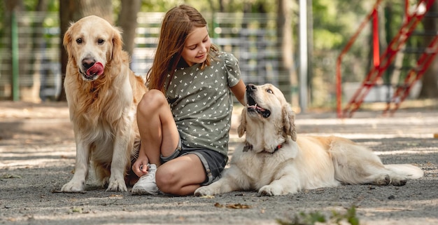 Preteen dziewczyna pieszczoty golden retriever w parku. Słodkie dziecko z psimi zwierzętami siedzącymi na zewnątrz