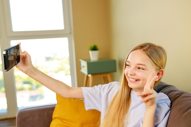 Preteen dziewczyna robi zdjęcia selfie na swoim smartfonie w przytulnym salonie w domu