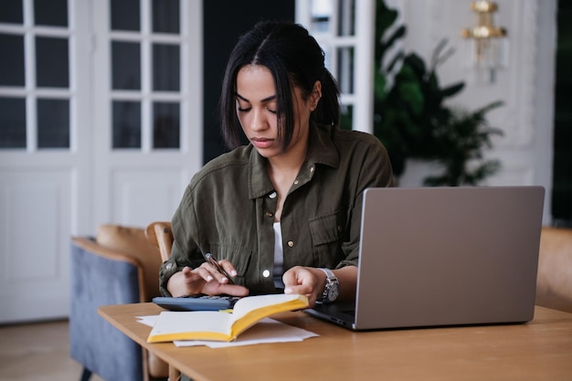 Pretty African American ?adna studentka dziewczyna siedzi przy biurku z pamiętnikiem laptopa u?ywa kalkulatora