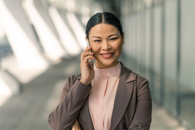 Pretty Businesswoman Uśmiecha Się Rozmawiając Na Telefon Komórkowy Przeciwko Centrum Biznesu Na Niewyraźne