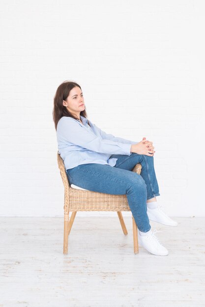 Pretty plus size model kobieta w koszuli i dżinsach pozowanie Studio na krześle, białe tło z miejsca kopiowania.