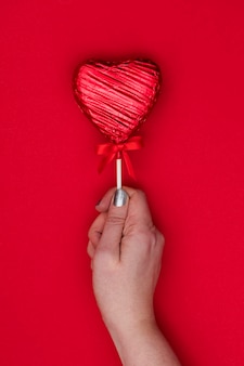Prezent walentynkowy kobieca ręka trzymająca lolla w kształcie serca na czerwonym tle