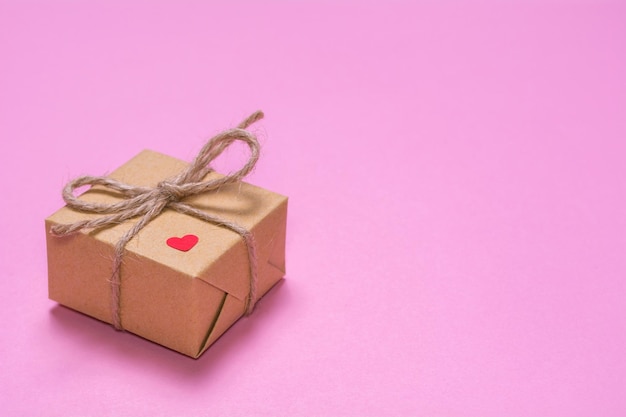 Prezent zawinięty w papier kraft na różowym tle Papierowe czerwone serce na pudełku prezentowym