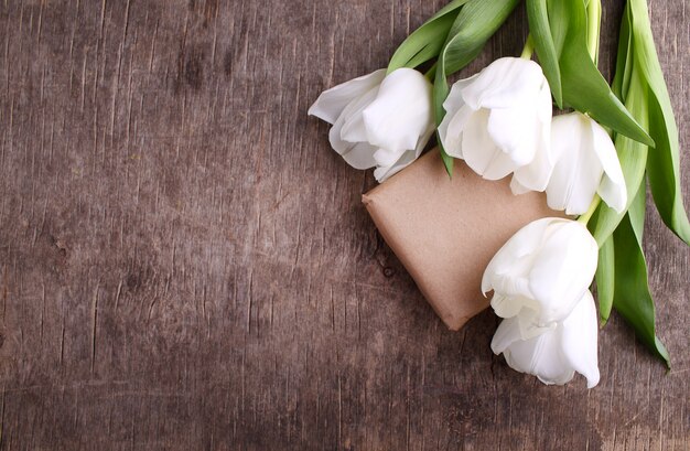 Prezenta pudełko z kwiatami na nieociosanym drewnianym tle (biali tulipany)