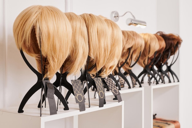 Prezentacja naturalnie wyglądających peruk w różnych kolorach przymocowanych do metalowych uchwytów peruk w salonie piękności Rząd manekinów z różnymi odcieniami włosów na półce w sklepie z perukamixA